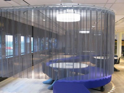 A small table with three chairs and a part of purple sofa is surrounded by chain link curtain.