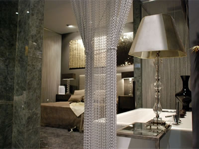 White chain link curtain as room divider in the hotel room, and there is a bed, several lamps, a table in it.